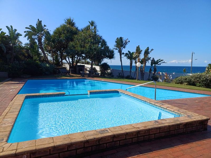 A well-maintained outdoor swimming pool and raised spa area featuring brick paving, metal handrails, and scenic ocean views.