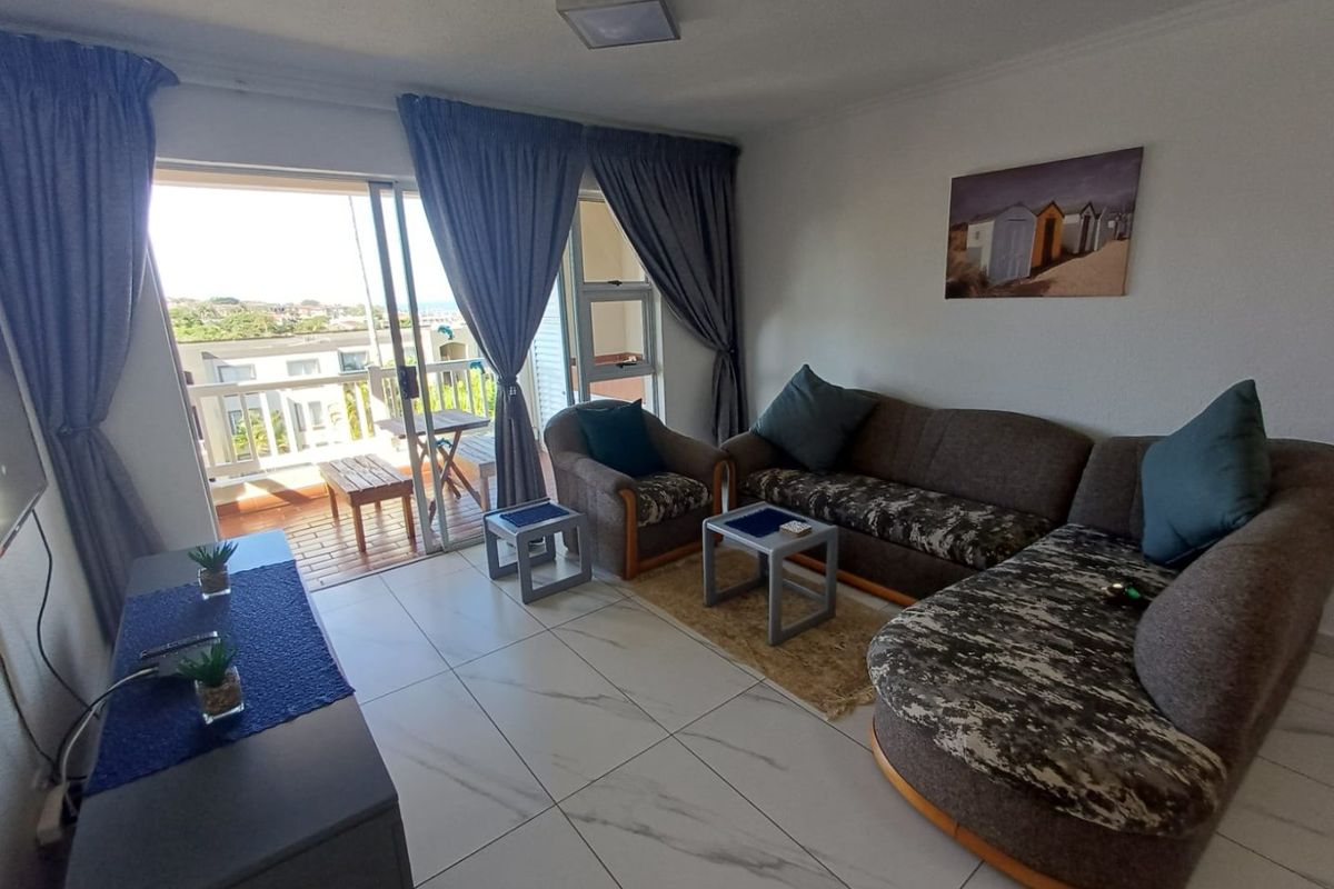 A bright living room featuring large format tiled flooring and a sliding glass door that opens onto a private balcony with exterior views.