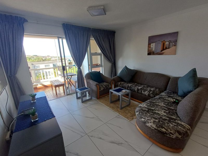 A bright living room featuring large format tiled flooring and a sliding glass door that opens onto a private balcony with exterior views.