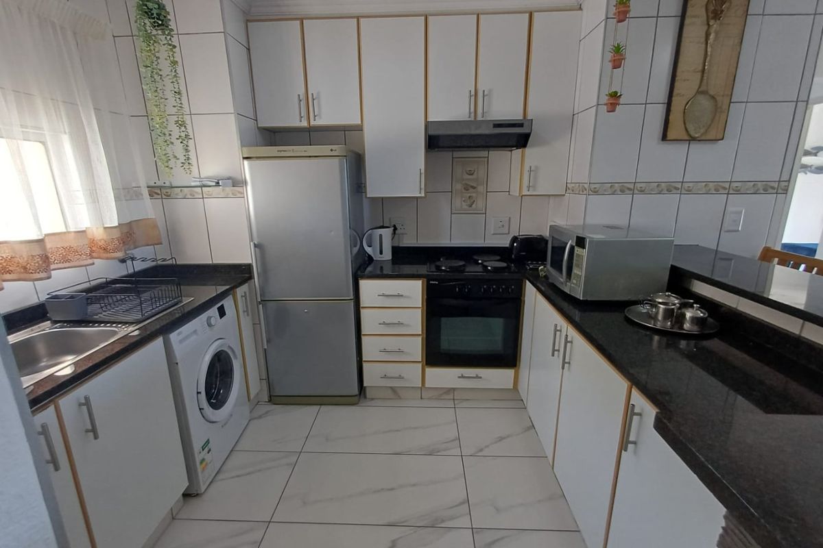 A functional kitchen featuring white cabinetry, granite countertops, tiled flooring, and integrated appliances including an oven and hob.