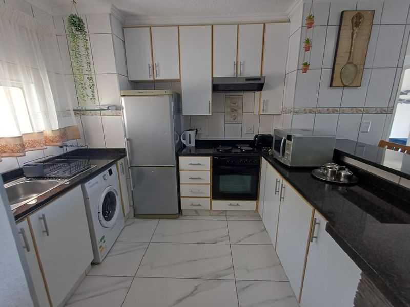 A functional kitchen featuring white cabinetry, granite countertops, tiled flooring, and integrated appliances including an oven and hob.