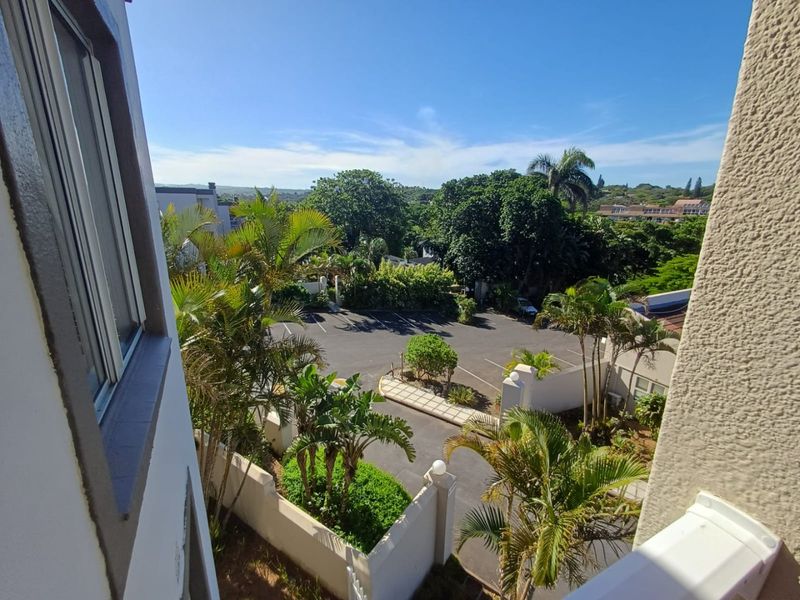 Elevated view from the balcony overlooking the complex parking area, landscaped gardens, and surrounding neighborhood.