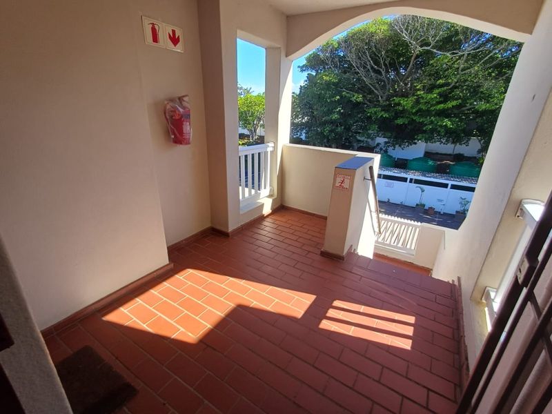 A covered outdoor balcony or landing area featuring terracotta tiled flooring, safety railings, and a wall-mounted fire extinguisher.