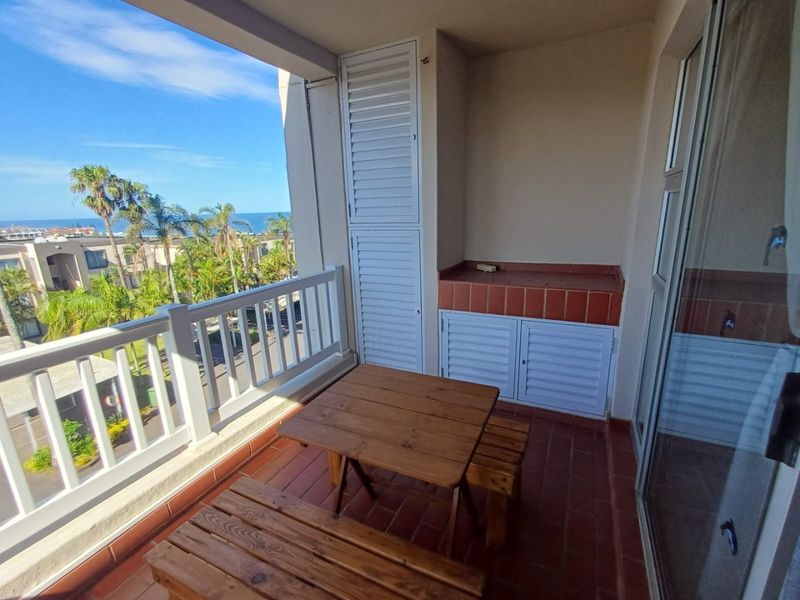 A covered balcony featuring tiled flooring, built-in storage, and a built-in counter, offering pleasant views of the surrounding area and distant ocean.