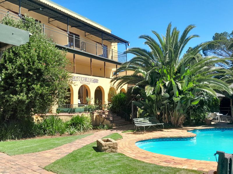 Outdoor pool area featuring a swimming pool, brick paving, landscaped garden, and a multi-level building with an arched veranda and balcony.