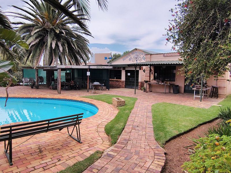 Outdoor entertainment area featuring a swimming pool, brick paved patio, and covered seating space set within a landscaped garden.