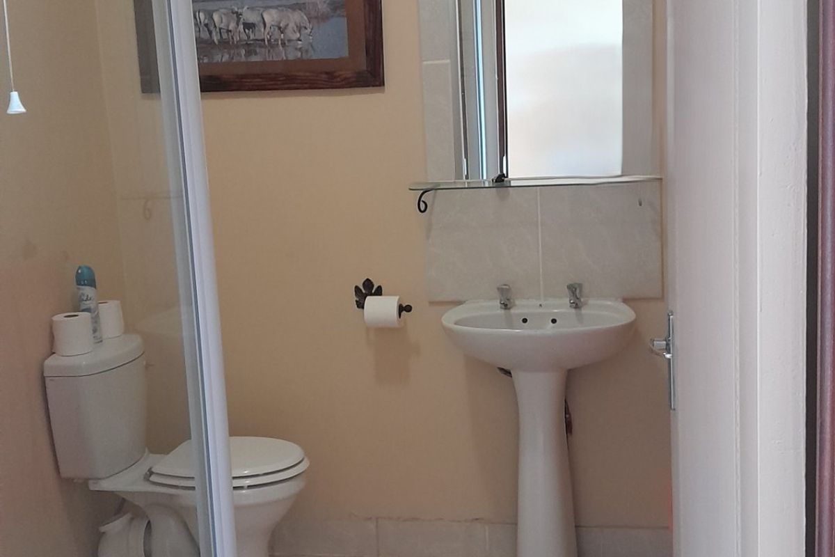 A functional bathroom featuring a pedestal basin, toilet, and a glass-enclosed shower, finished with neutral wall tones and standard flooring.