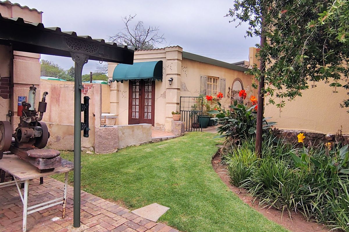 A rear garden view featuring a brick-paved patio area, a covered structure, and a small building with french doors and a green awning.