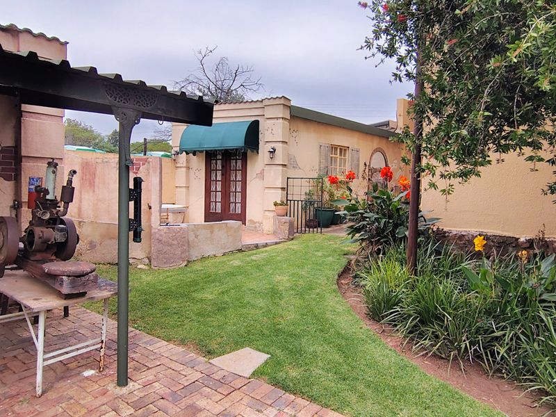 A rear garden view featuring a brick-paved patio area, a covered structure, and a small building with french doors and a green awning.