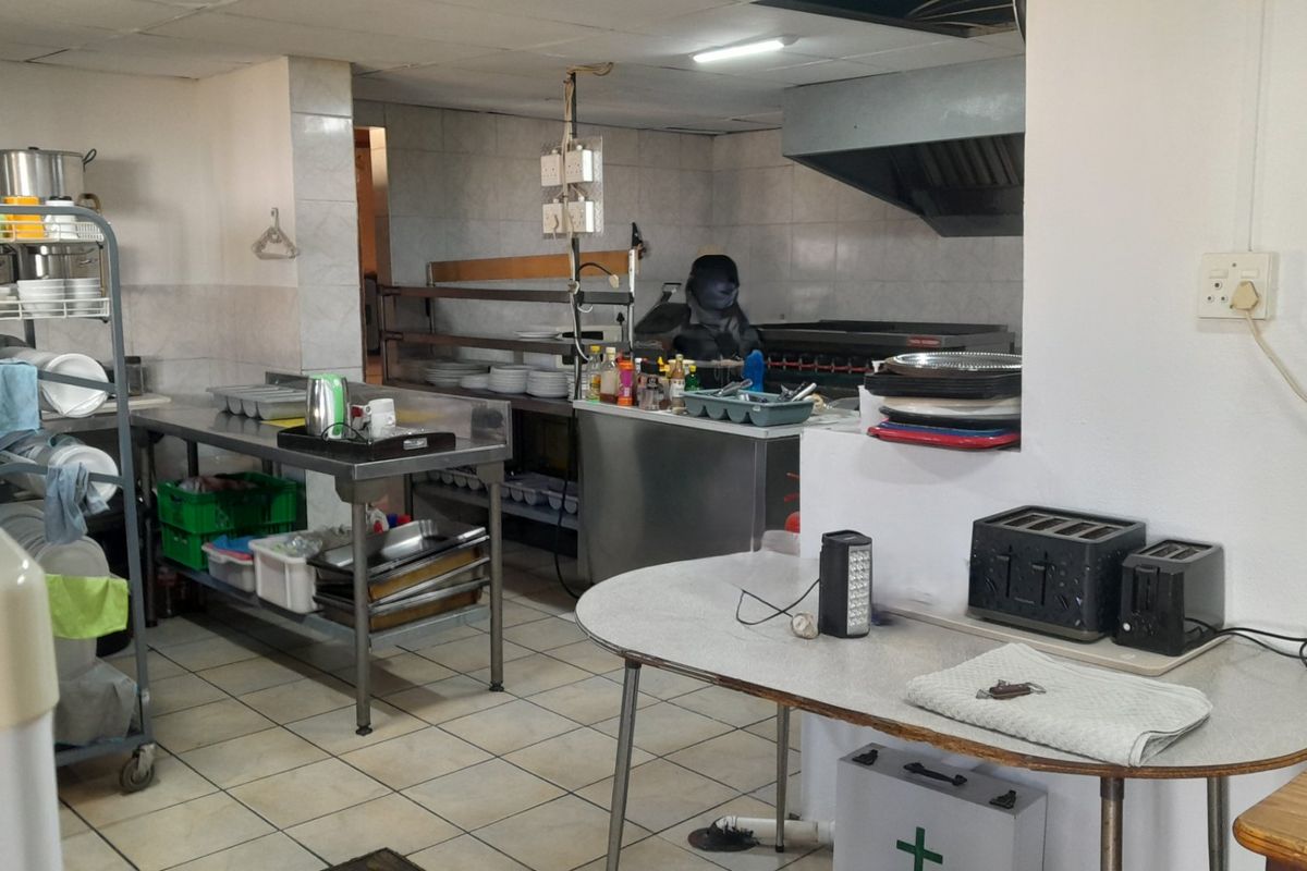 A functional commercial-style kitchen featuring stainless steel prep surfaces, tiled flooring, and an integrated extractor hood, suitable for high-volume food preparation.