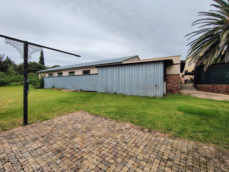 Rear exterior view of the property featuring a corrugated metal structure, brick accents, a paved patio area, and a surrounding lawn.