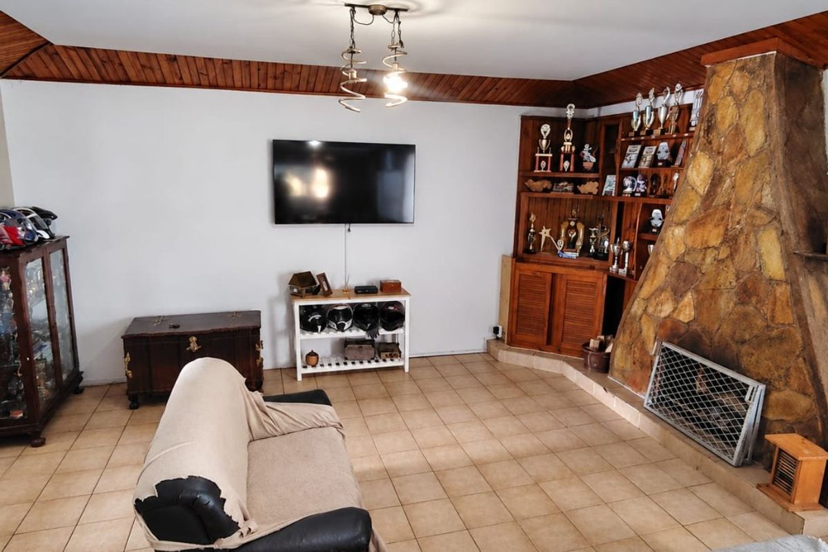 A living room featuring a prominent stone fireplace, built-in wooden display cabinetry, and tiled flooring with timber ceiling detailing.