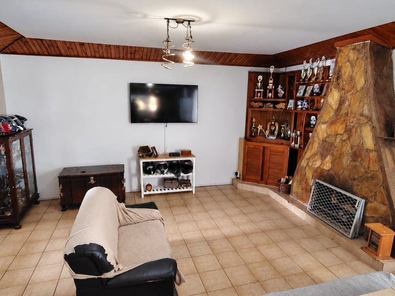 A living room featuring a prominent stone fireplace, built-in wooden display cabinetry, and tiled flooring with timber ceiling detailing.