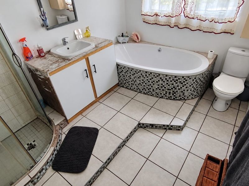 A functional bathroom featuring a built-in bathtub with mosaic tile surround, a separate shower enclosure, a toilet, and a vanity unit with a basin.