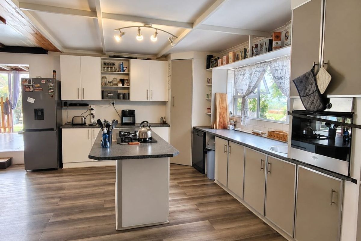 A well-lit kitchen featuring a central island, built-in oven, gas hob, and ample cabinetry, finished with modern laminate flooring and exposed ceiling beams.