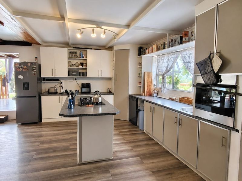 A well-lit kitchen featuring a central island, built-in oven, gas hob, and ample cabinetry, finished with modern laminate flooring and exposed ceiling beams.