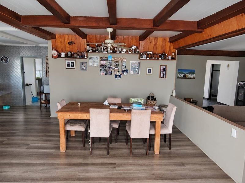 Open plan dining area featuring exposed timber ceiling beams, wood-paneled feature wall, and modern laminate flooring, creating a warm and connected living space.