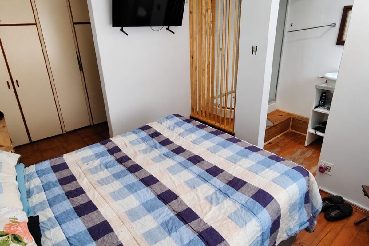 Bedroom featuring built-in cupboards, original wooden flooring, and an open-plan en-suite bathroom area with a decorative timber screen.