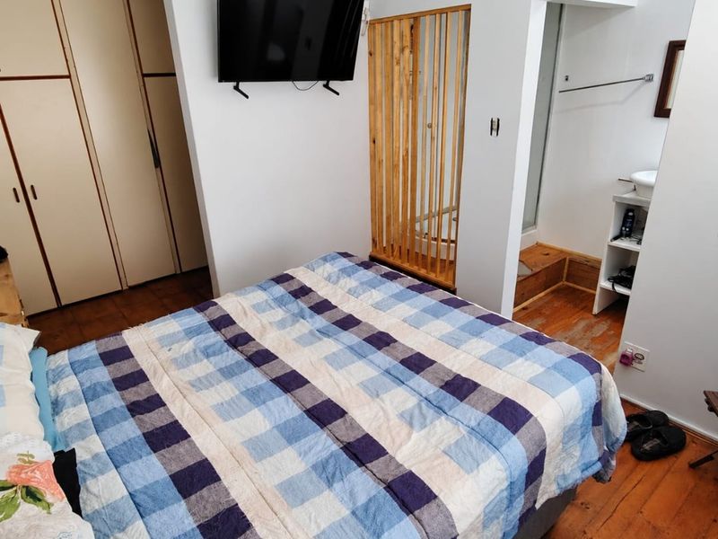 Bedroom featuring built-in cupboards, original wooden flooring, and an open-plan en-suite bathroom area with a decorative timber screen.