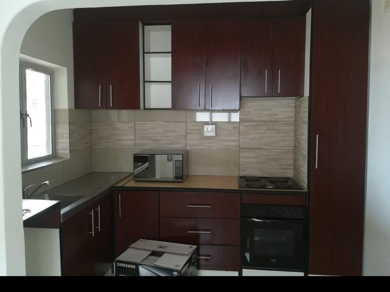 A functional kitchen featuring dark wood cabinetry, integrated oven and hob, tiled backsplash, and ample storage space with a tall pantry unit.