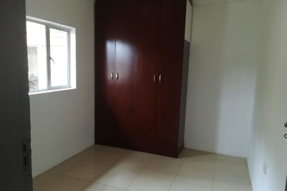 A simple, empty bedroom featuring tiled flooring and a built-in wooden wardrobe.