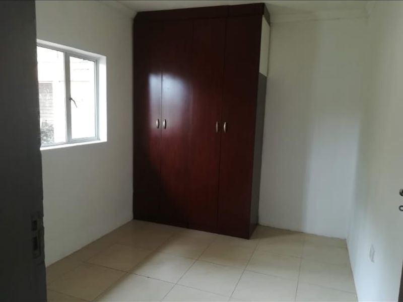 A simple, empty bedroom featuring tiled flooring and a built-in wooden wardrobe.