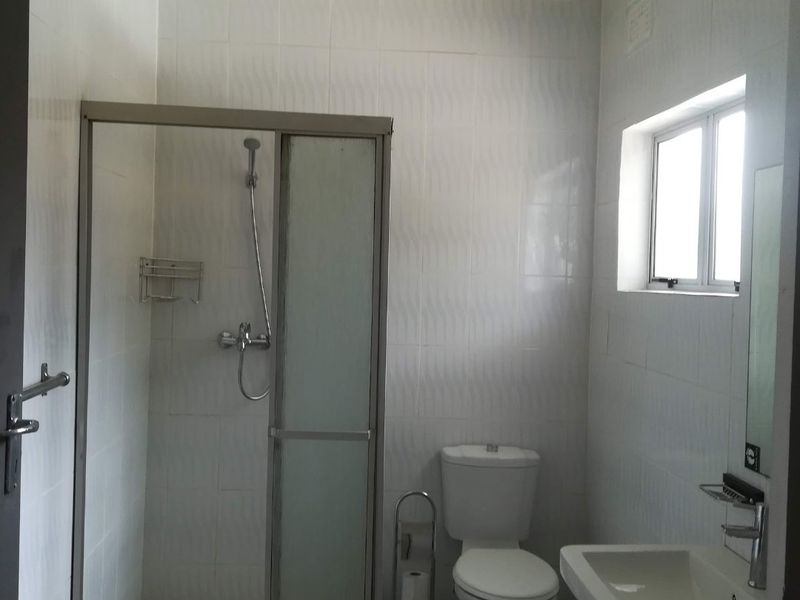 A functional bathroom featuring a shower enclosure, pedestal basin, and toilet with neutral wall and floor tiling.