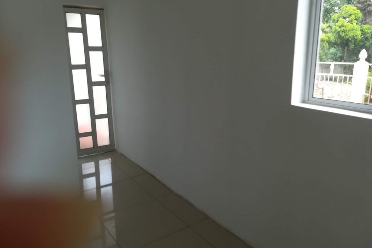 A bright, empty hallway featuring neutral tiled flooring, a modern glass-panelled door, and a window providing natural light.