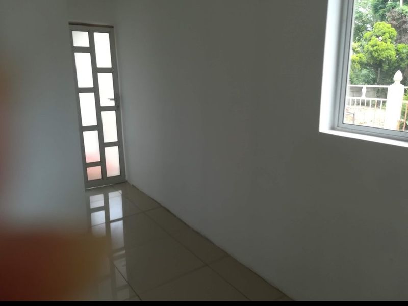 A bright, empty hallway featuring neutral tiled flooring, a modern glass-panelled door, and a window providing natural light.