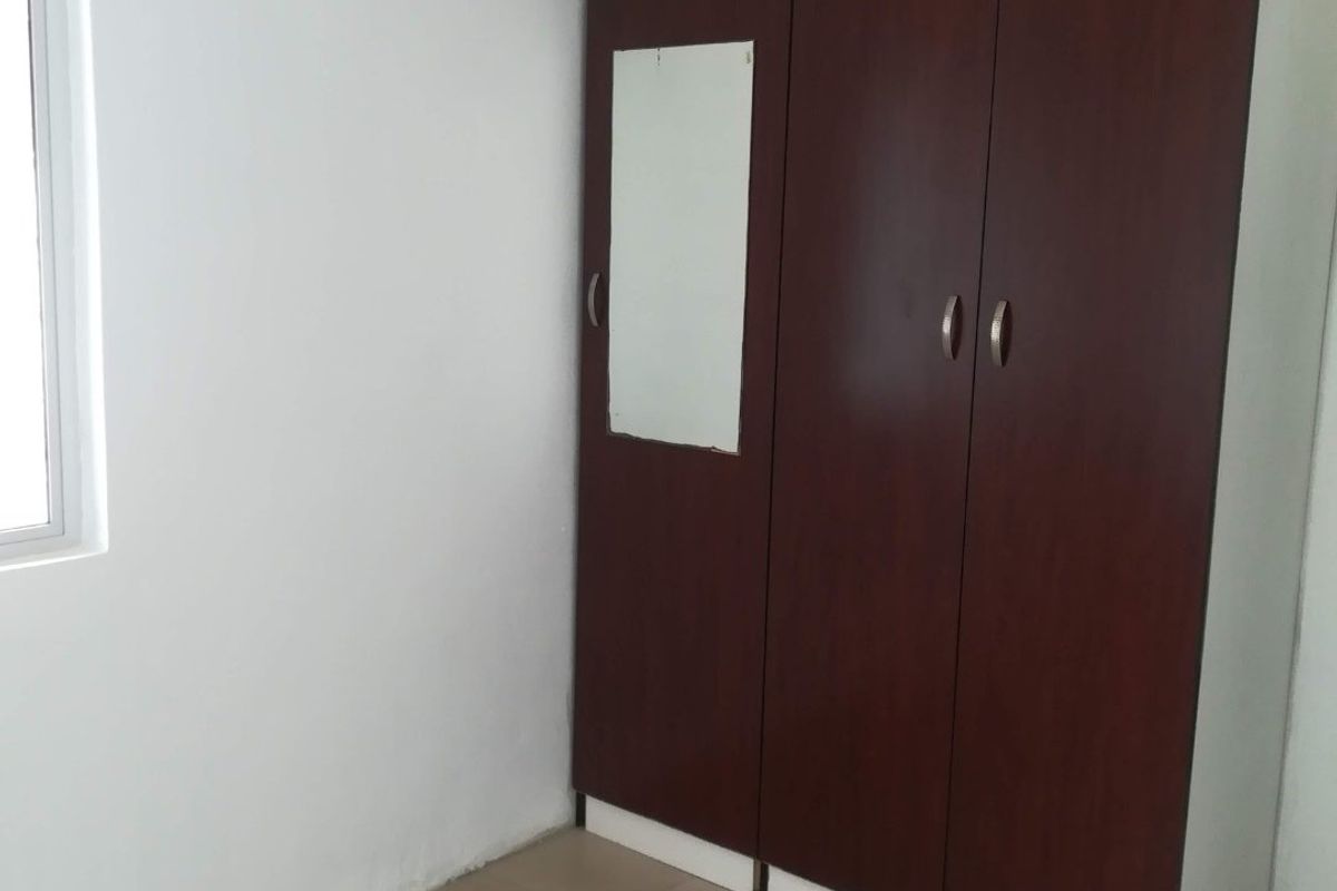 A clean, empty bedroom featuring neutral tiled flooring, white walls, and a dark wood-finish built-in wardrobe with a small integrated mirror.