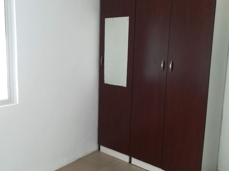 A clean, empty bedroom featuring neutral tiled flooring, white walls, and a dark wood-finish built-in wardrobe with a small integrated mirror.