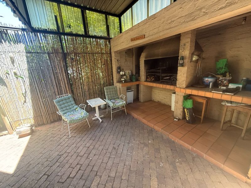 Covered outdoor patio area featuring a built-in braai, brick flooring, and bamboo privacy screening, offering a rustic space for outdoor entertainment.