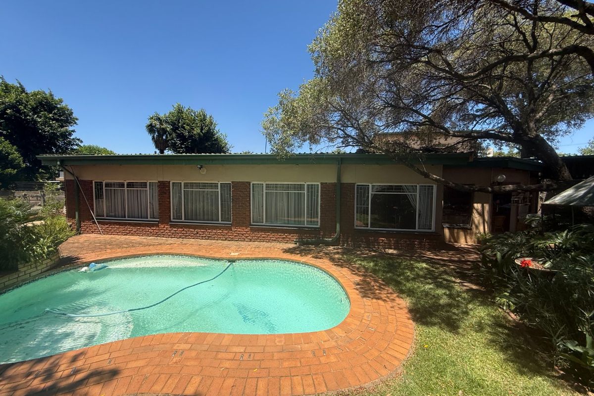 Rear exterior view of the house featuring a swimming pool, brick paved surround, and established garden area.