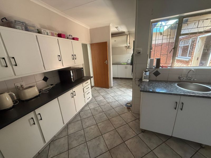 A functional kitchen featuring white cabinetry, dark laminate countertops, tiled flooring, and a secondary scullery area visible through the doorway.