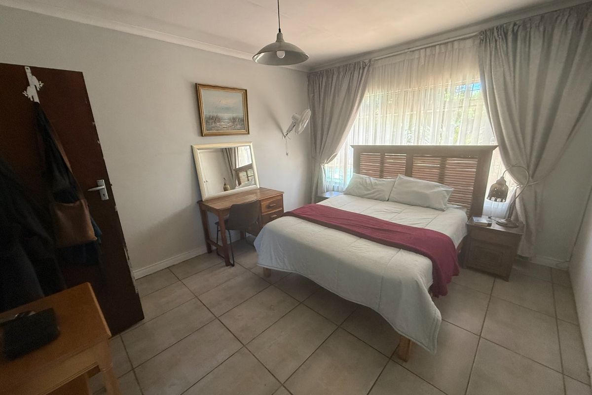 A functional bedroom featuring tiled flooring, neutral wall finishes, and large windows with curtain treatments, providing a comfortable and well-lit living space.