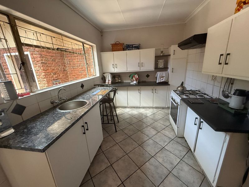 Functional kitchen featuring white cabinetry, dark laminate countertops, gas hob, extractor fan, and tiled flooring with a large window overlooking the exterior.