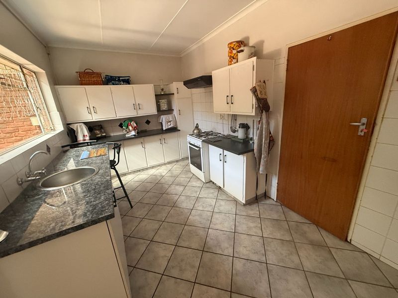 A functional kitchen featuring built-in cabinetry, laminate countertops, a gas stove with extractor fan, and tiled flooring throughout.