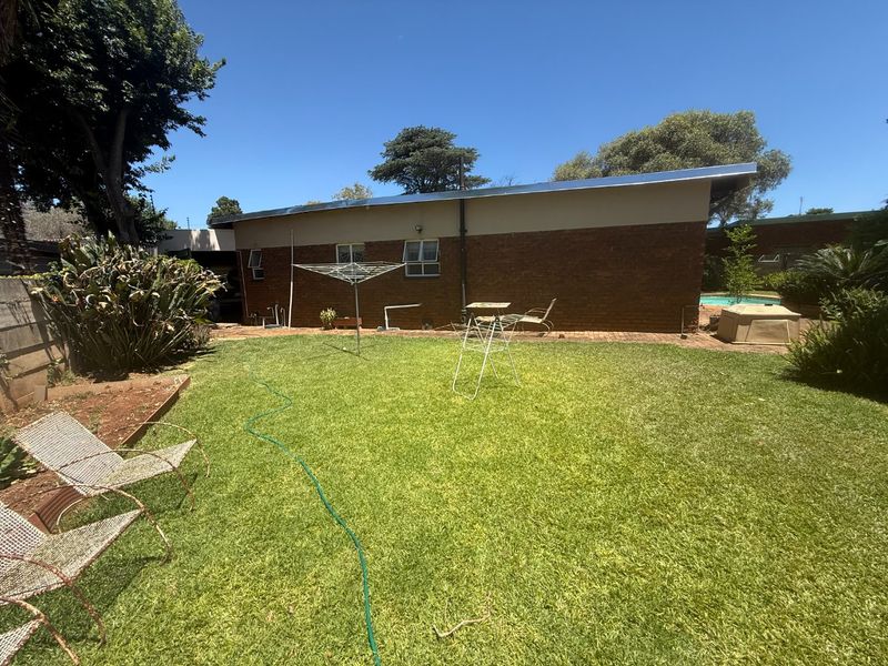 Rear view of the property featuring a brick facade, a well-maintained lawn, and a swimming pool in the background.