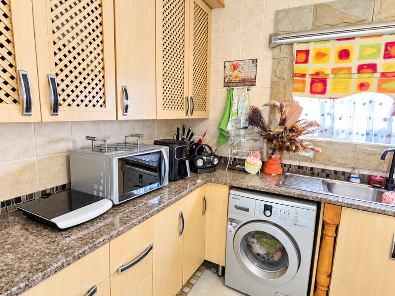 A functional kitchen featuring light wood cabinetry, granite countertops, a tiled backsplash, and an integrated washing machine with decorative ceiling detailing.