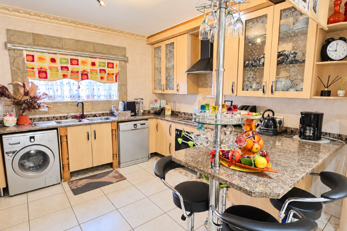 A functional kitchen featuring light wood cabinetry, granite countertops, a breakfast bar, and integrated appliances with tiled flooring throughout.
