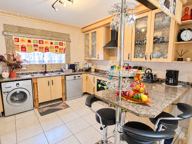 A functional kitchen featuring light wood cabinetry, granite countertops, a breakfast bar, and integrated appliances with tiled flooring throughout.