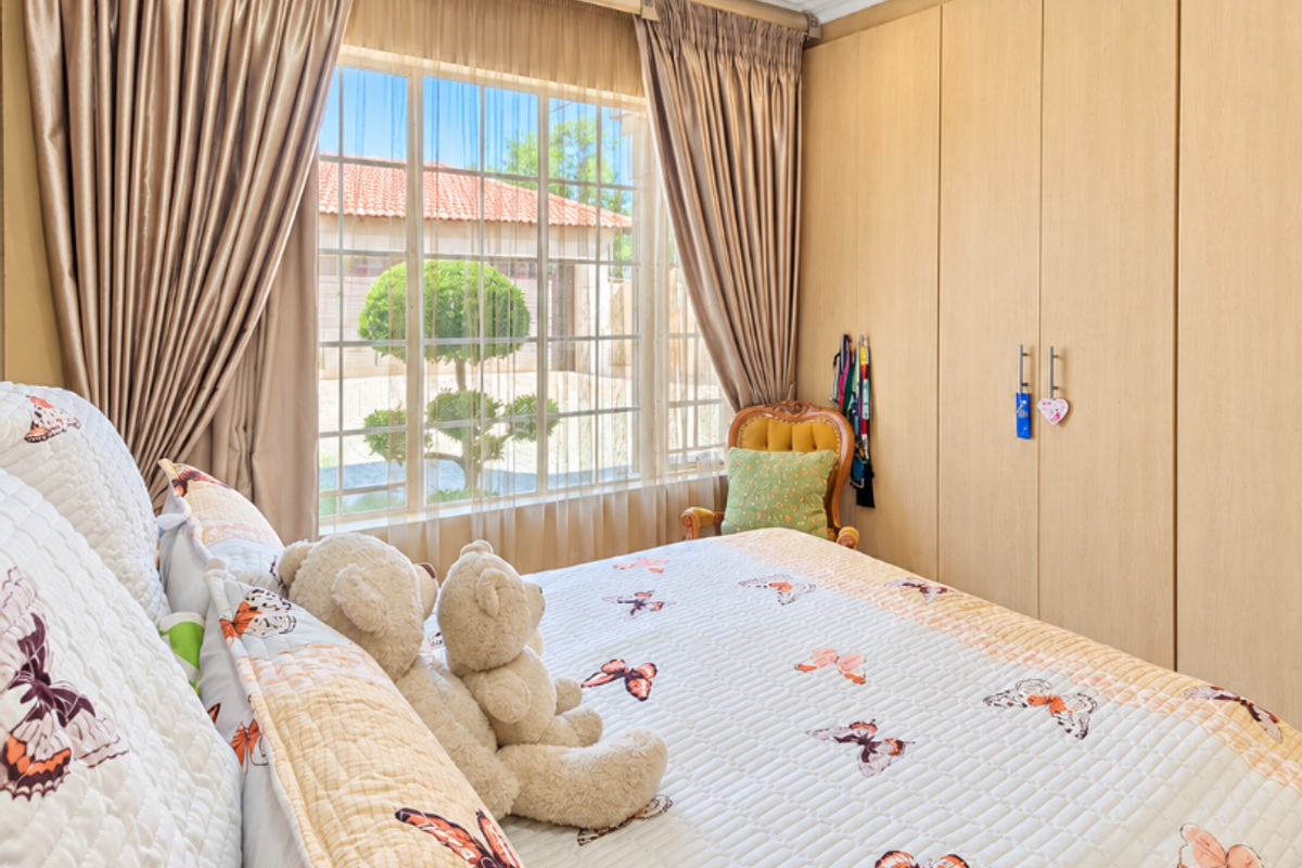 A well-maintained bedroom featuring built-in wooden cupboards, recessed downlighting, and large windows with curtains, offering a bright and comfortable living space.