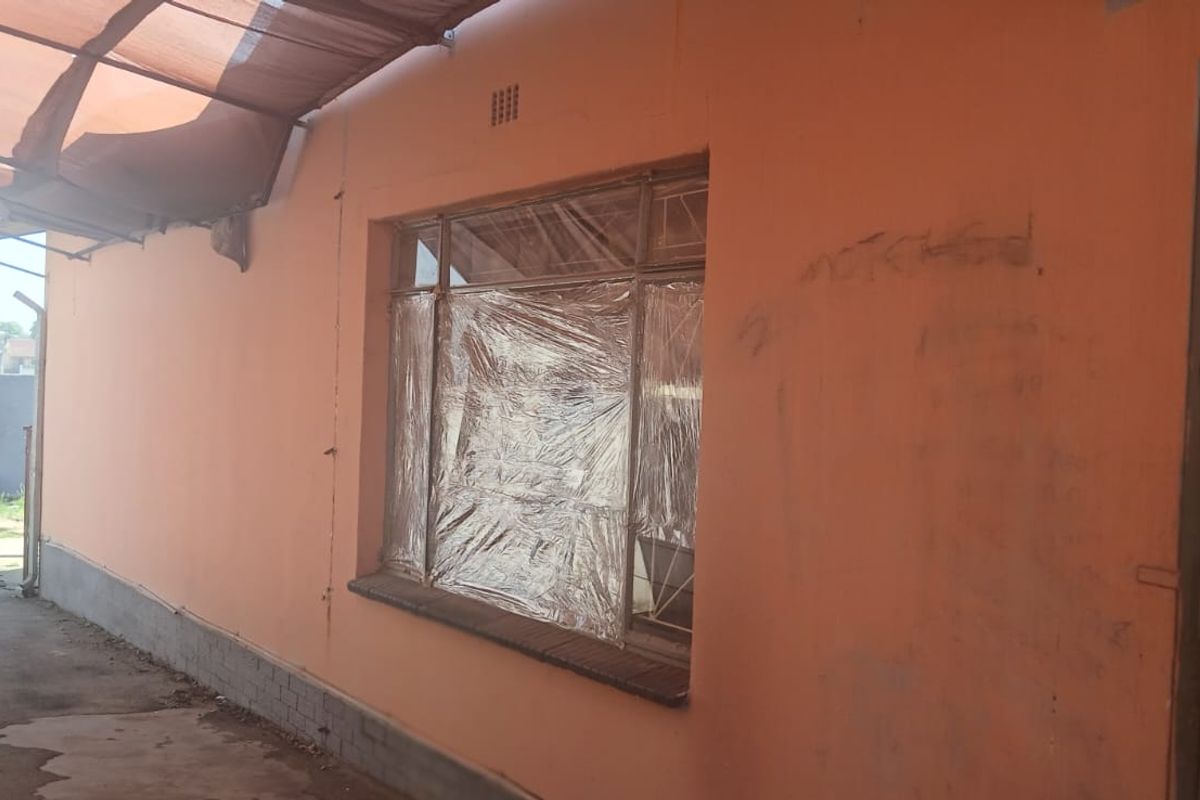 Rear exterior view of the property featuring a covered patio area, security gate, and window with damaged finishes and visible wall graffiti.