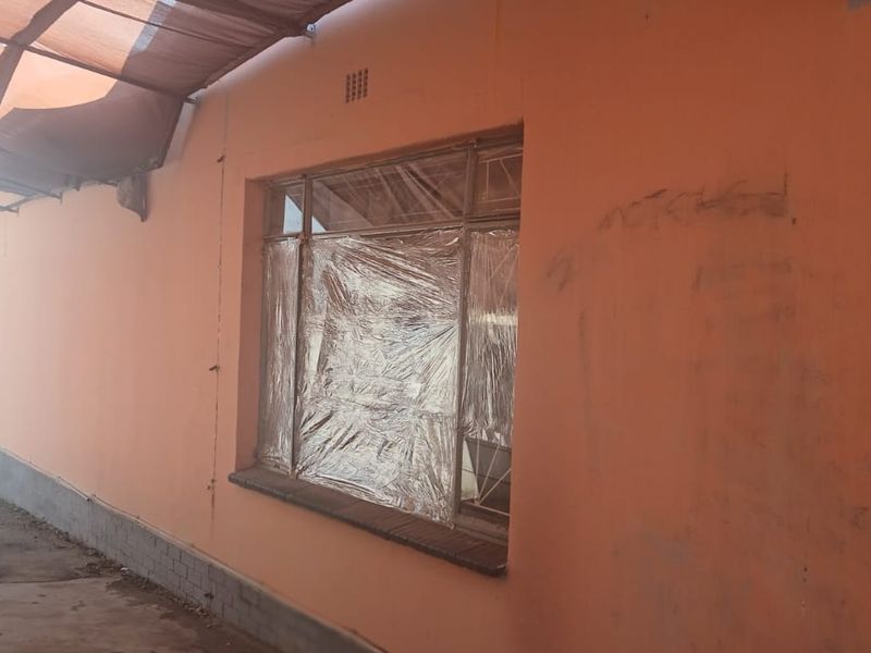 Rear exterior view of the property featuring a covered patio area, security gate, and window with damaged finishes and visible wall graffiti.