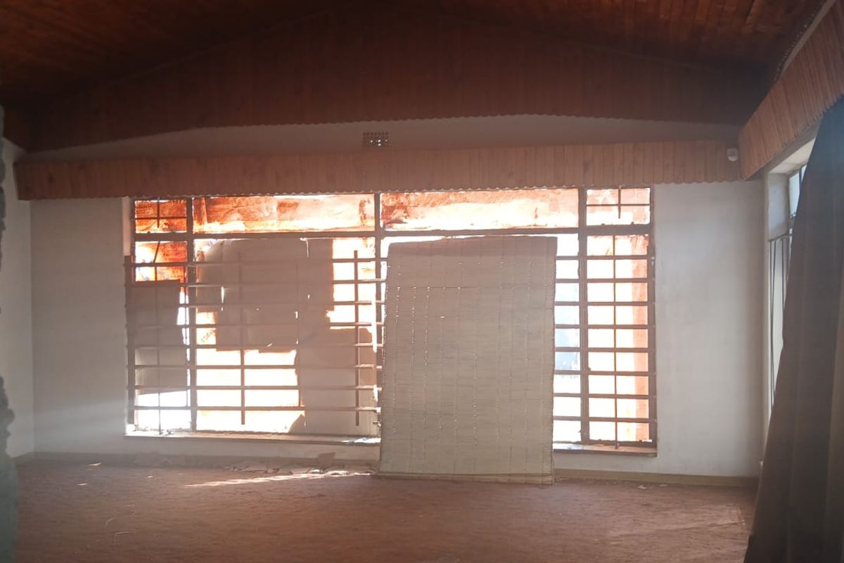Spacious living area featuring a vaulted timber-clad ceiling and large steel-framed windows, requiring renovation to restore its original character.