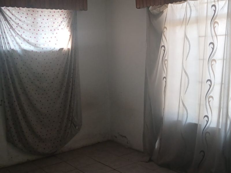 A vacant bedroom featuring tiled flooring and window security bars, showing signs of wall surface wear and potential damp issues requiring maintenance.