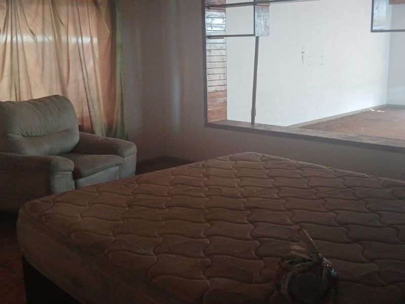 A bedroom featuring tiled flooring and a large window looking into an adjacent space, requiring cosmetic updates to improve its overall appeal.