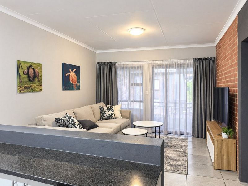 An open-plan living area featuring a striking exposed brick wall, tiled flooring, and a sliding glass door leading to a balcony.