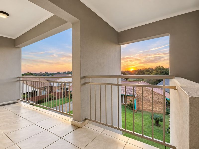 A spacious covered balcony featuring tiled flooring and a metal balustrade, offering elevated views of the surrounding residential area at sunset.