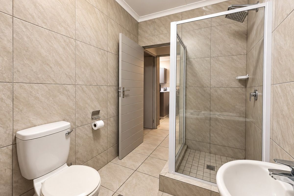 Modern bathroom featuring a glass-enclosed shower with a rain shower head, tiled walls and flooring, a toilet, and a wash basin.
